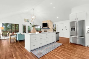 A modern kitchen with a stone fireplace, white cabinetry, and a large stainless steel refrigerator.