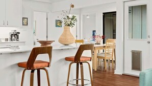 A modern kitchen with white cabinetry, a central island with stools, and a dining area with chairs.