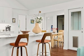 A modern kitchen with white cabinetry, a central island with stools, and a dining area with chairs.