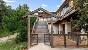A wooden staircase leading to a building with a balcony, surrounded by greenery.