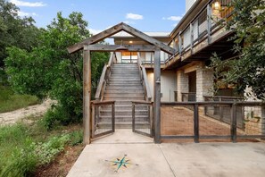 A wooden staircase leading to a building with a balcony, surrounded by greenery.