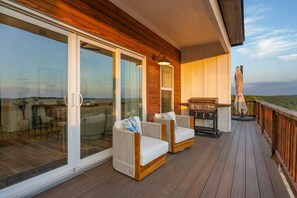 Eine Terrasse mit zwei weißen Sitzgelegenheiten, einem Grill und einer Glastür zum Patio.
