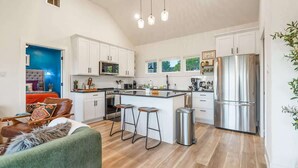 A modern kitchen with white cabinets, a stainless steel refrigerator, and a bar stool.