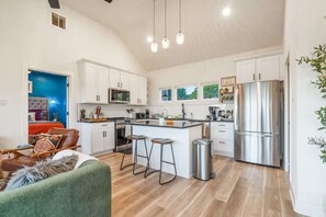 A modern kitchen with white cabinets, a stainless steel refrigerator, and a bar stool.