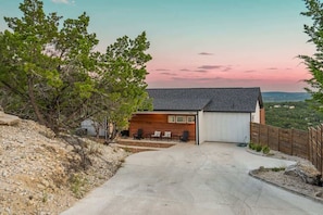Ett modernt hus med ett garage, en uteplats med stolar och en uppfart som leder fram till garaget.