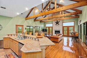 A spacious kitchen with a large island, wooden beams, and a fireplace. - Star House | Private Views • Hill Country Comfort (Wimberley)