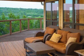A covered outdoor seating area with wicker furniture and cushions, overlooking a forested landscape. - Star House | Private Views • Hill Country Comfort (Wimberley)