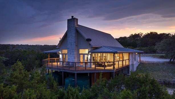 Ein modernes Haus mit einer großen Terrasse, einem Steinkamin und Blick auf den umliegenden Wald.