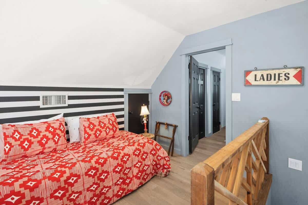Une chambre à coucher avec un lit, une échelle, une pancarte indiquant « DAMES » et une porte donnant sur une autre pièce.