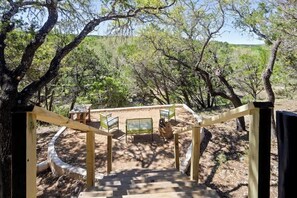 Una escalera de madera lleva a un espacio de descanso con sillas y una mesa, rodeado de árboles.