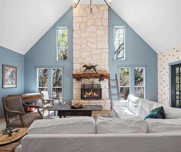 Una habitación acogedora con chimenea de piedra, un sofá blanco y una zona de comedor con sillas.