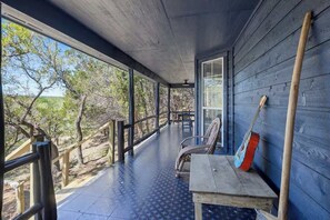 Une véranda couverte avec une rambarde en métal, une table, des chaises et une guitare appuyée contre le mur.