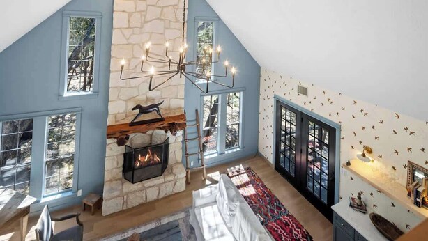 Un espacio tipo loft con chimenea de piedra, ventanas amplias y una araña.