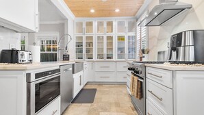 Una cocina moderna con armarios blancos, electrodomésticos de acero inoxidable y techo de madera.