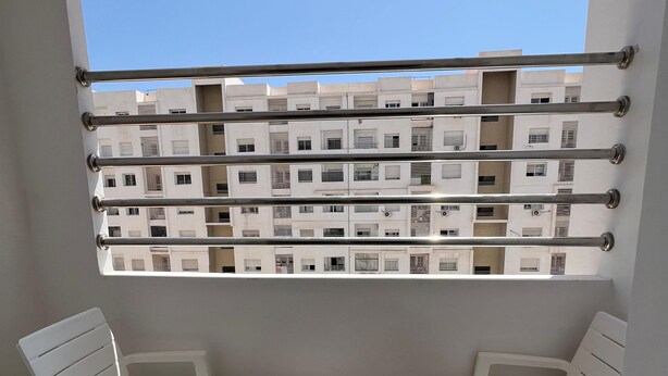 Un balcon avec des chaises en plastique blanches et une petite table, donnant sur une rangée de bâtiments blancs.