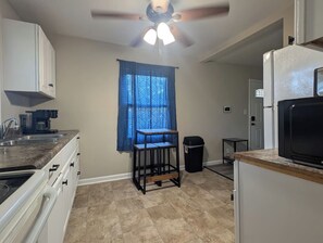 A kitchen with a built-in stove, a sink, a ceiling fan, and a window with patterned curtains.