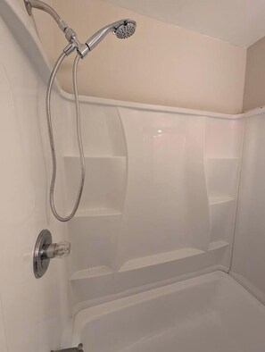 Et hjørne af et badeværelse med en bruseniche, toilet og håndvask.