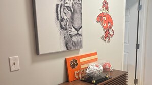 A room with a framed tiger portrait, a sports-themed wall decal, and a wooden console table with decorative items. - Delightful 1-bedroom condo in Clemson. (Clemson)
