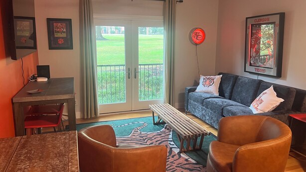 A living room with a couch, chairs, a table, and a bench. There is a door leading to a balcony with a view of a green lawn. - Delightful 1-bedroom condo in Clemson. (Clemson)