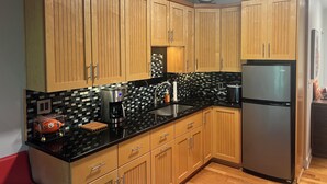 A kitchen with wooden cabinets, a black countertop, a stainless steel refrigerator, and a tiled backsplash. - Delightful 1-bedroom condo in Clemson. (Clemson)