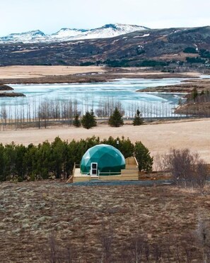 A geodesic dome structure in a natural setting with a river and mountains in the background. - Golden Circle Domes - Lake View (Selfoss)