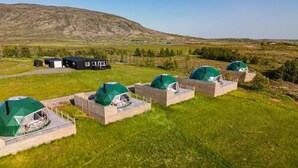 A row of dome-shaped tents with wooden platforms, set in a grassy field with a mountain in the background. - Golden Circle Domes - Lake View (Selfoss)