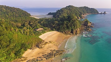 Una vista aerea di una zona costiera con spiaggia, costa rocciosa e colline ricoperte da una fitta vegetazione.