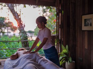 A person performing a massage on a bed in a room with wooden walls and a view of greenery outside. - Wa Ale Resort (We Ale Island)