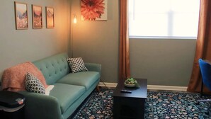En stue med en tealgrøn sofa, et mønstret tæppe og et stort blomsterbillede på væggen.
