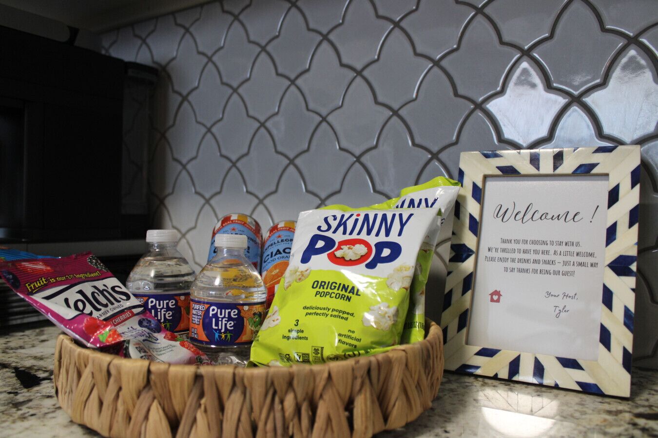 A kitchen counter with a basket containing snacks, a bottle of water, and a bag of Skinny Pop popcorn.