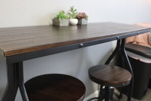 A dark wooden table with a metal frame, two round stools, and small potted plants on a white wall.