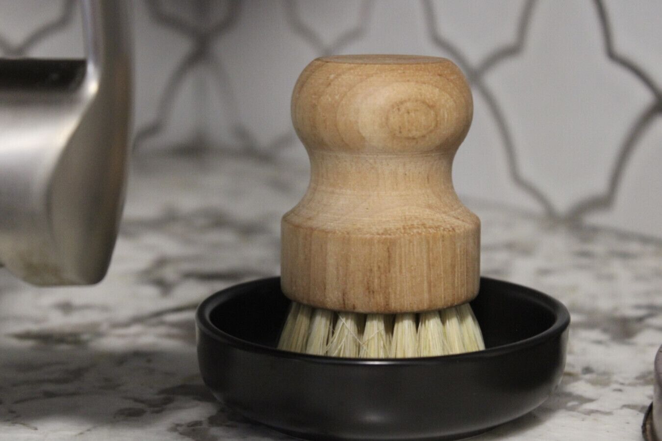 A wooden brush in a black bowl on a marble countertop.