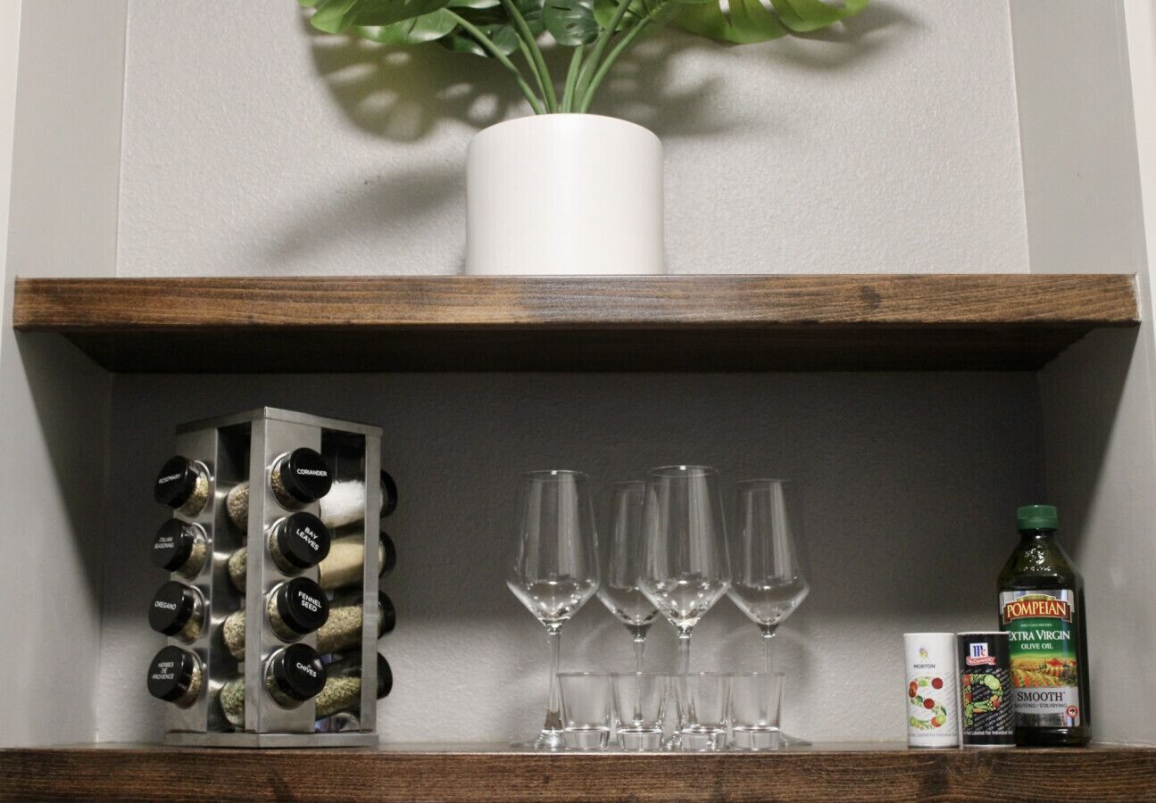 Una estantería con una botella de vino, copas y un organizador de especias.