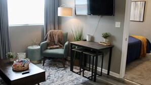 Una sala de estar con sofá, sillón, mesa de centro, televisor y una mesita de noche con lámpara.