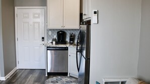 Cocina compacta con gabinetes blancos, electrodomésticos de acero inoxidable y un tapete estampado.