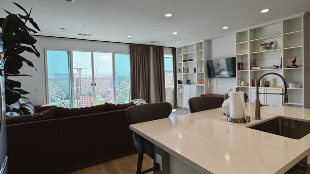 A modern kitchen with a central island, a dining area with a sofa, and a large window offering a city view. - •Charming One-Level Home • Feels Like Home (Menifee)