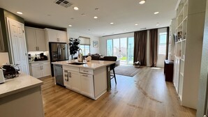 A modern kitchen with white cabinetry, a central island, and a dining area with a dark table and chairs. - •Charming One-Level Home • Feels Like Home (Menifee)