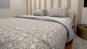 A modern bedroom with a large bed, striped wall, and a round side table. - •Charming One-Level Home • Feels Like Home (Menifee)