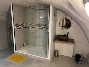 Een moderne badkamer met een douche in een glazen cabine, een houten wastafelmeubel met een ronde spiegel, en een kleine prullenbak.