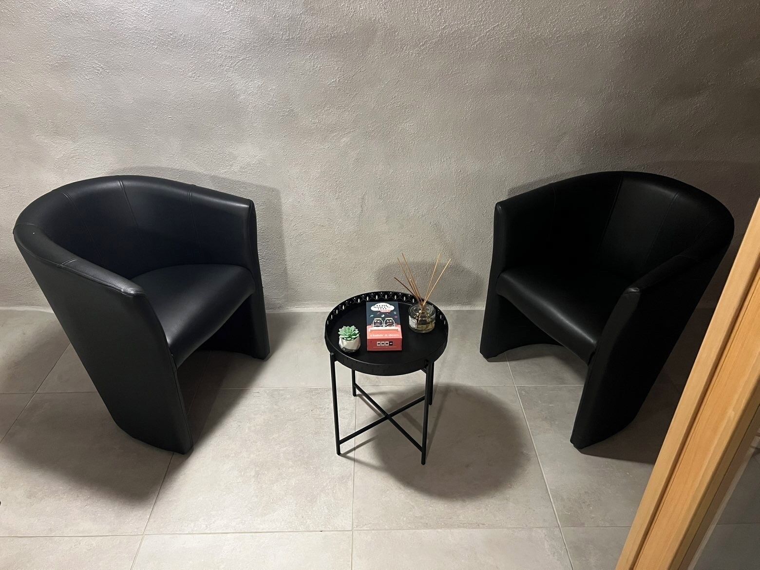 Two black chairs facing each other with a small table in between, containing a small plant, a candle, and a box.