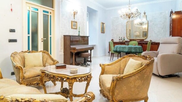 Ein geräumiges Wohnzimmer mit aufwendigen Möbeln, einem Klavier und einem Essbereich mit einer Chandelüster.