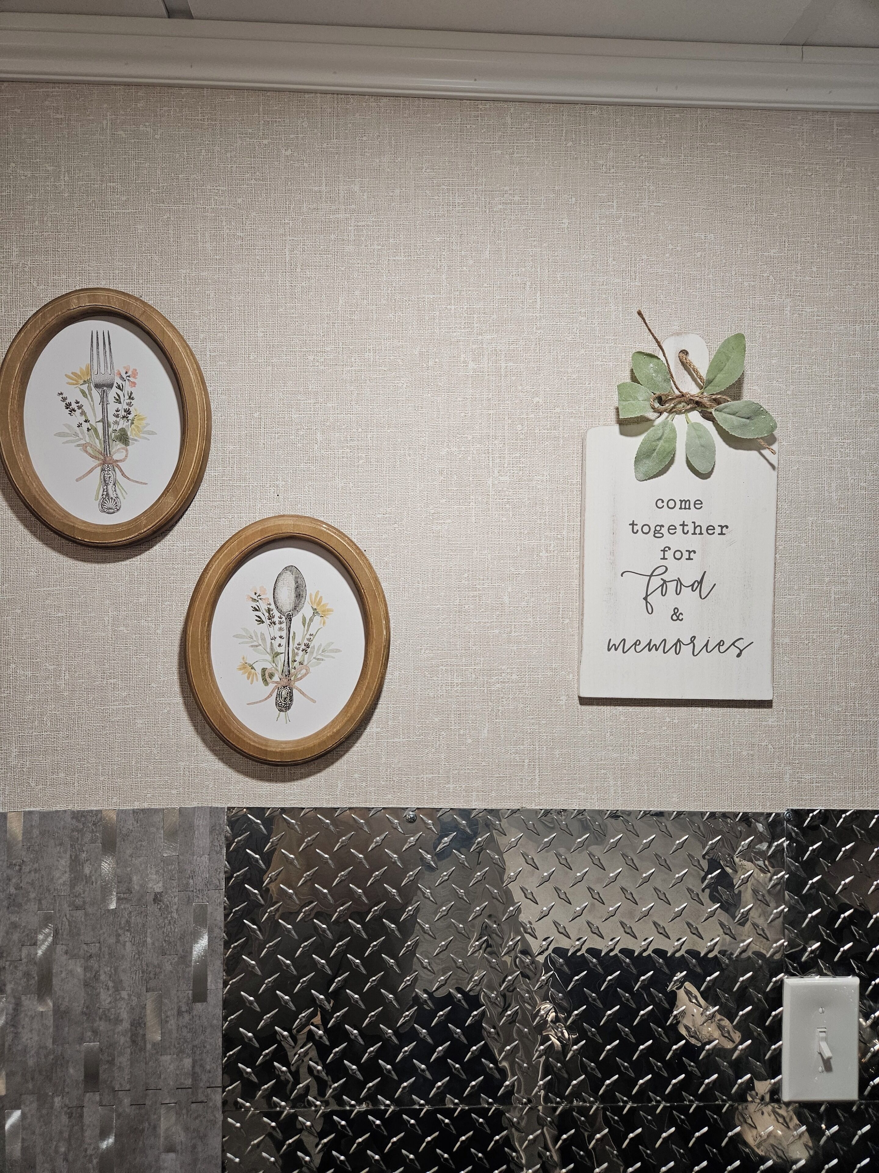 Eine Wand mit zwei gerahmten Bildern, eines zeigt eine Gabel und Blumen, das andere eine Botschaft über gemeinsames Essen und das Schaffen von Erinnerungen.