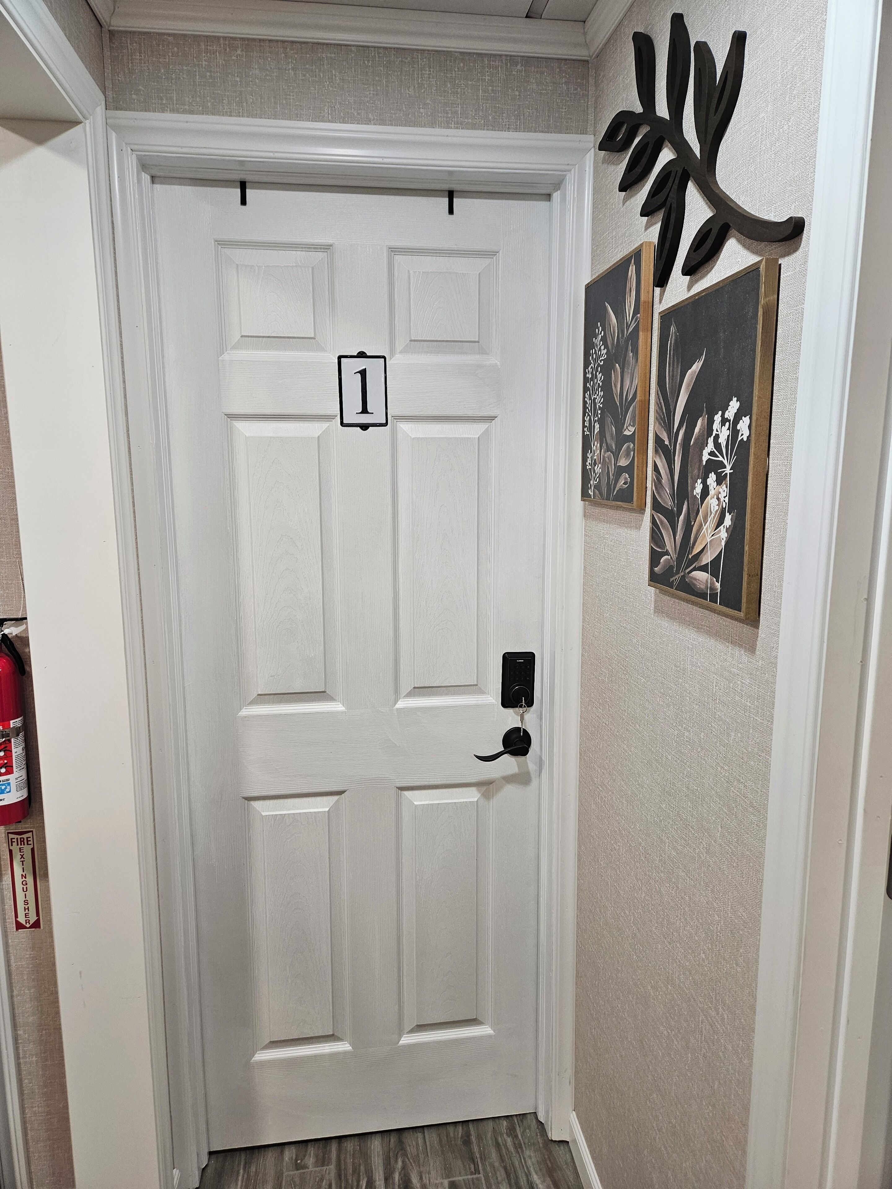Una puerta blanca con un letrero del número 1, un timbre y un extintor a la izquierda.