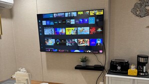 Een moderne keuken met een flatscreen-tv aan de muur, waarop diverse streamingdiensten worden getoond. Voor de tv staat een houten eettafel met een placemat en een kleine potplant.