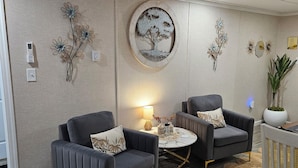 Een moderne woonkamer met twee grijze fauteuils, een ronde salontafel en een potplant.