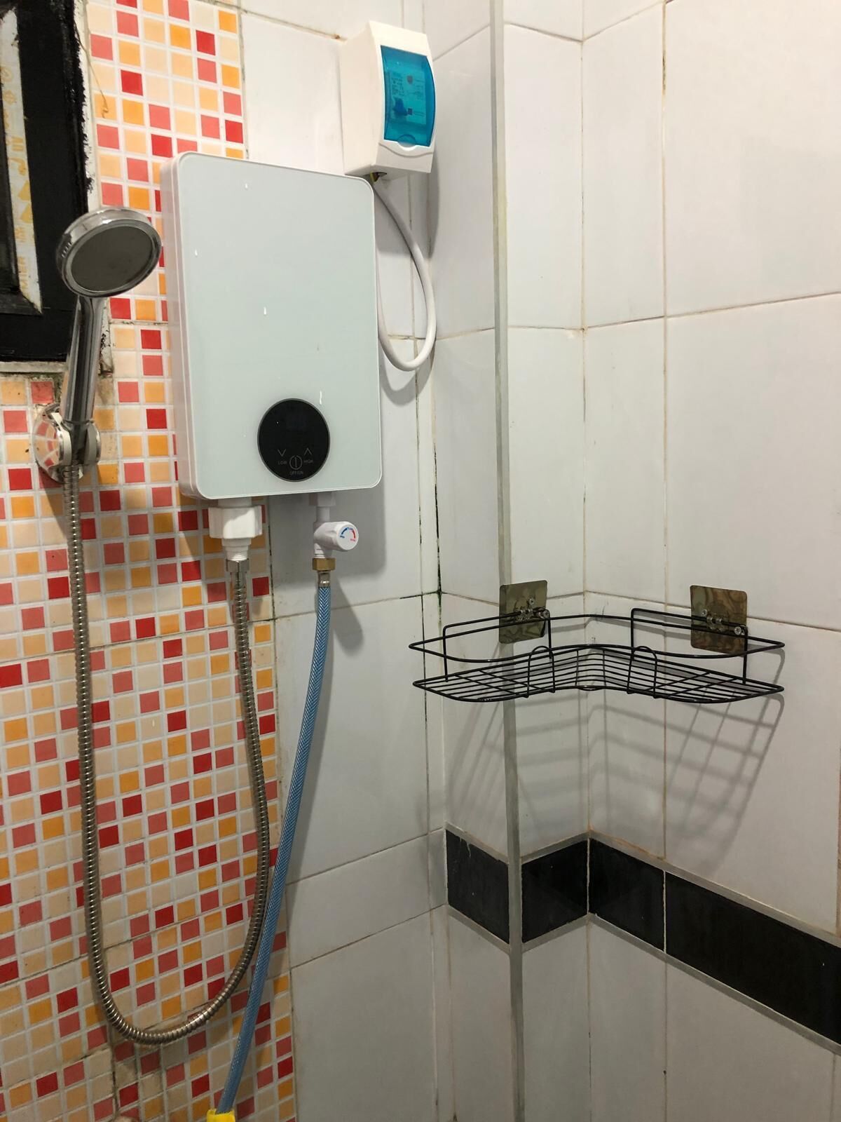 A shower with a handheld showerhead, a wall-mounted control panel, and a metal shelf.