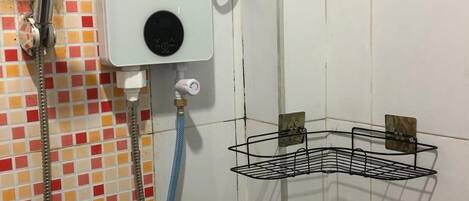 A shower with a handheld showerhead, a wall-mounted control panel, and a metal shelf.