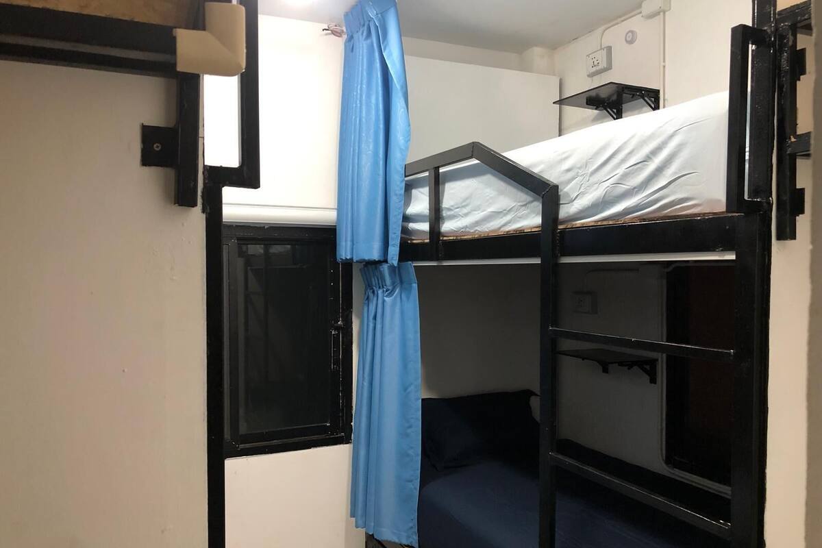 Habitación con literas, una ventana, una cortina y un estante pequeño.