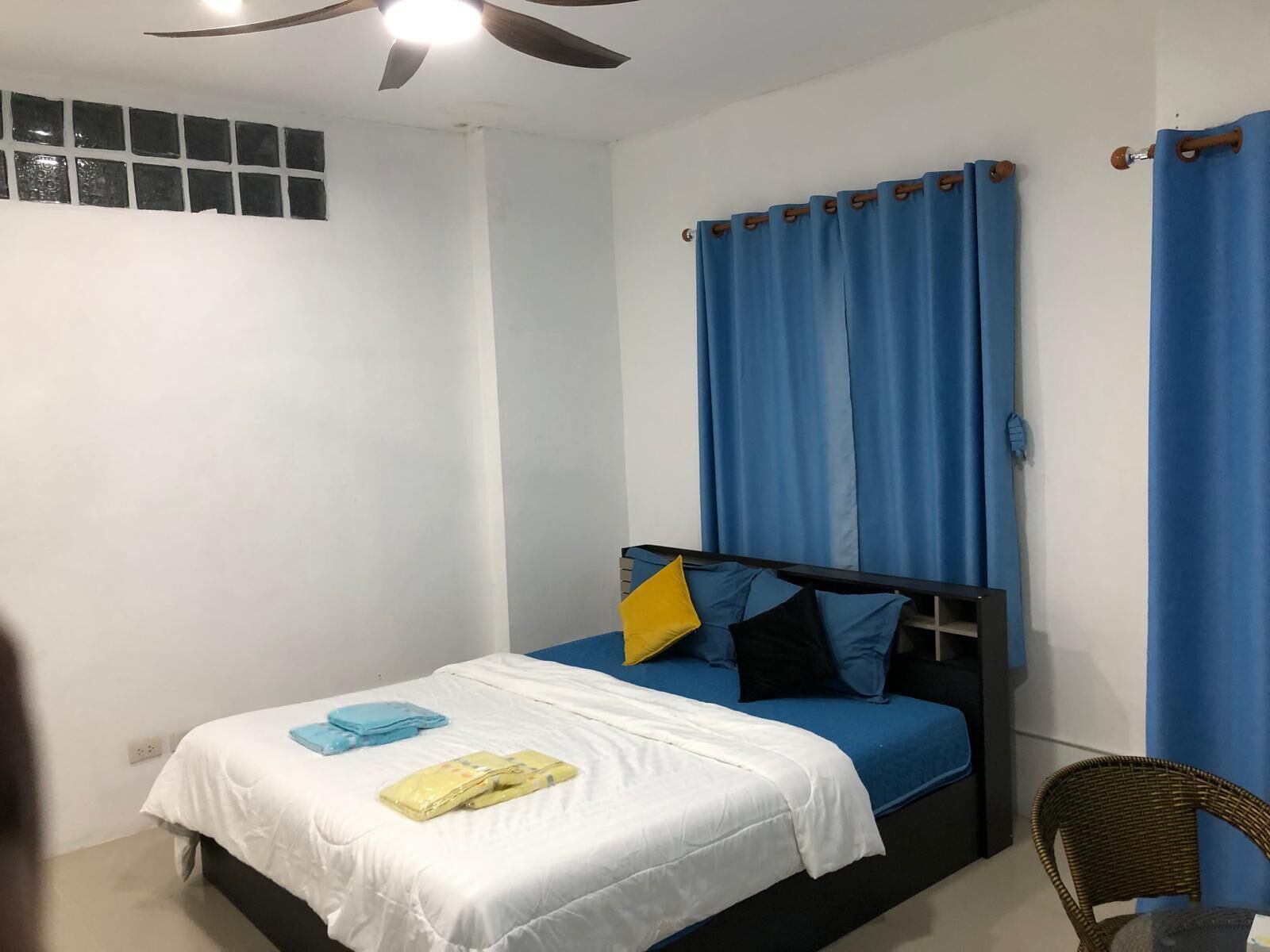 A bedroom with a bed, a ceiling fan, a window with blinds, and a chair.
