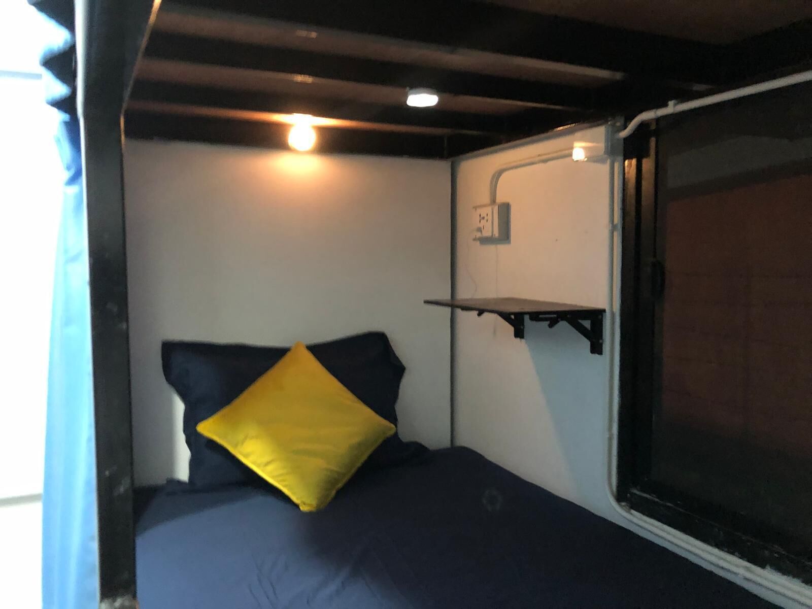 A small, compact room with a bed, a shelf, and a window.